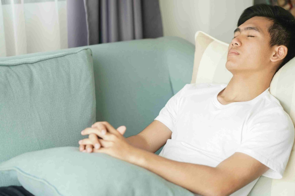 young man resting back on sofa with eyes closed