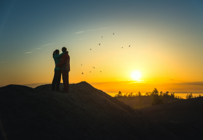 couple on mountain top embracing during sunset