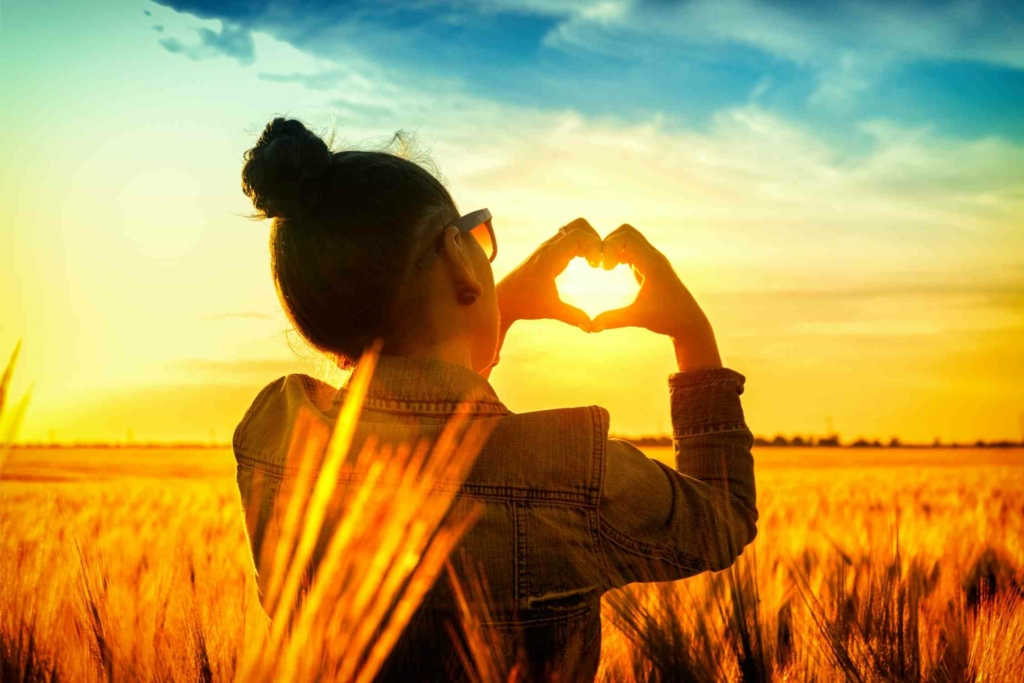 woman outside looking at sunset with hands in the shape of a heart