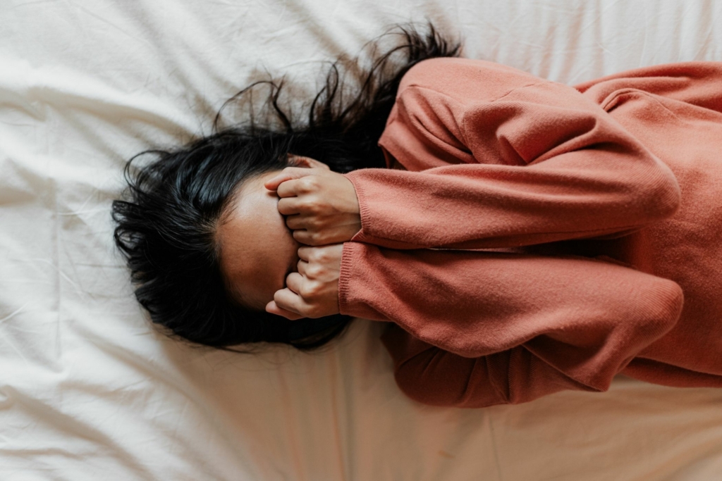 woman with hands over face in bed stressed