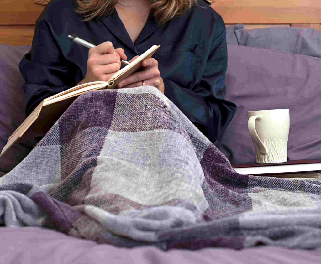 close up of woman in bed journaling with a cup of tea