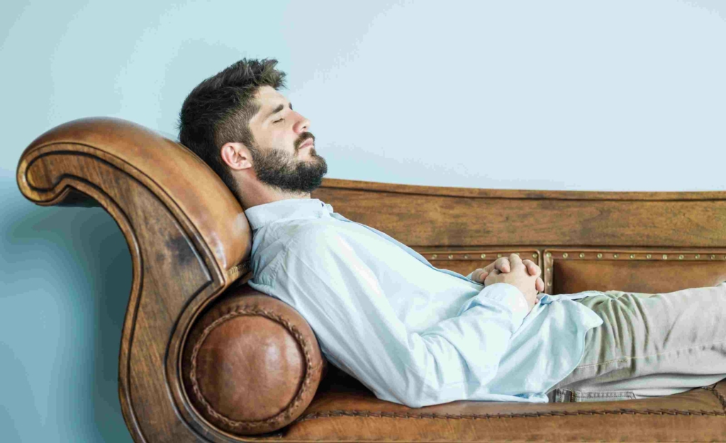 man with eyes closed resting on sofa during hypnosis session