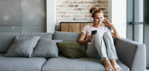 Woman on couch holding phone with headphones on