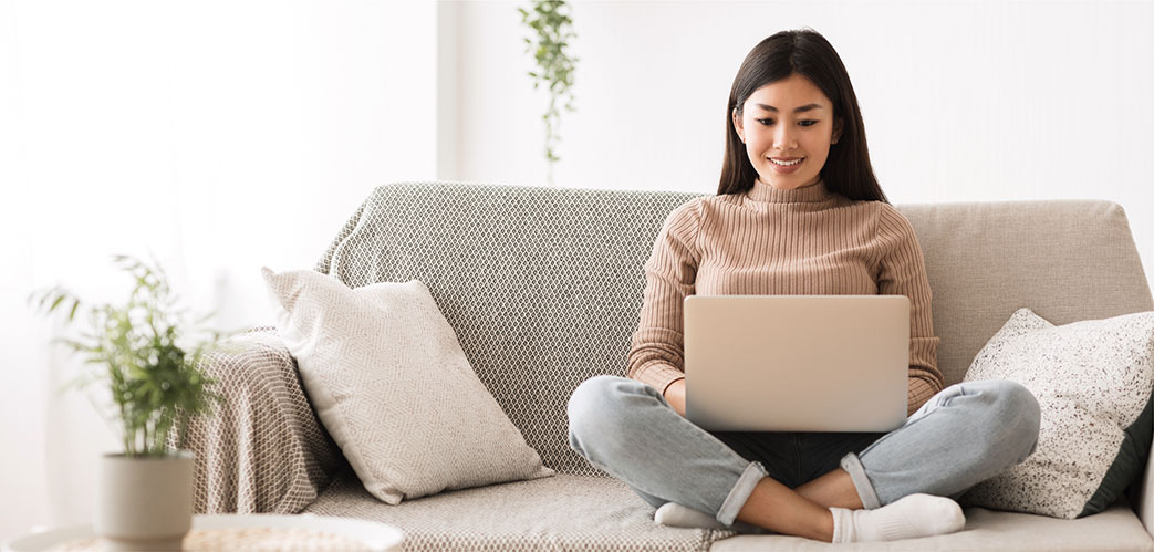 Woman sitting on sofa smiling looking at laptop