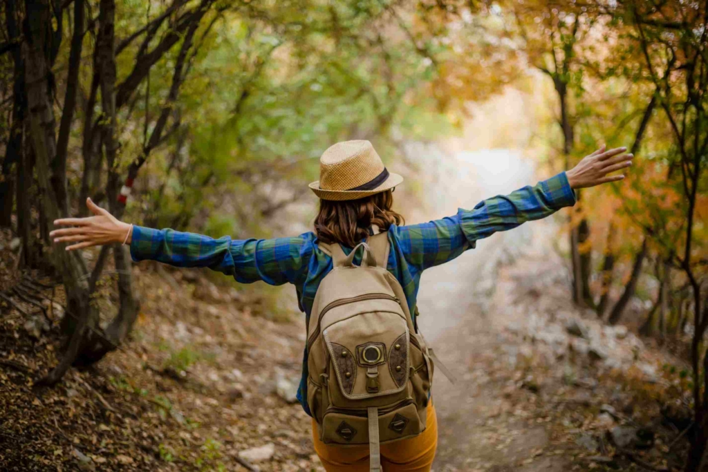 woman hiking in nature with backpack and arms outstretched