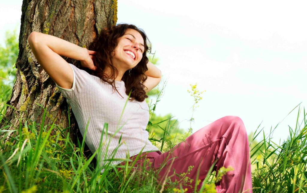 woman smiling and relaxing in nature leaning against a tree 