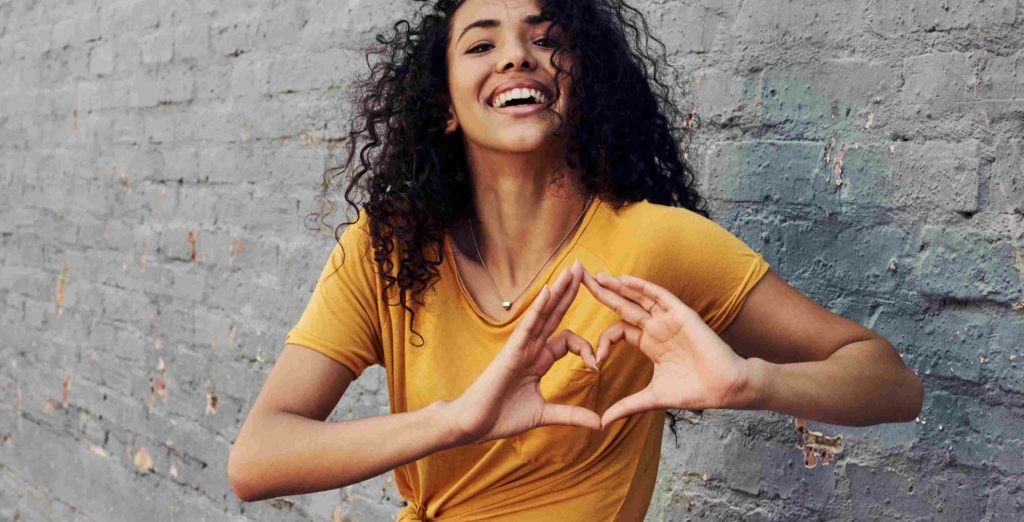 woman smiling with hands shaped as a heart over her heart